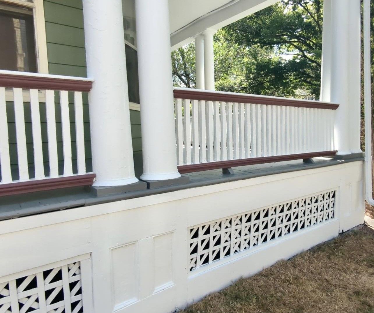White porch with decorative railing and geometric vents, brown trim.