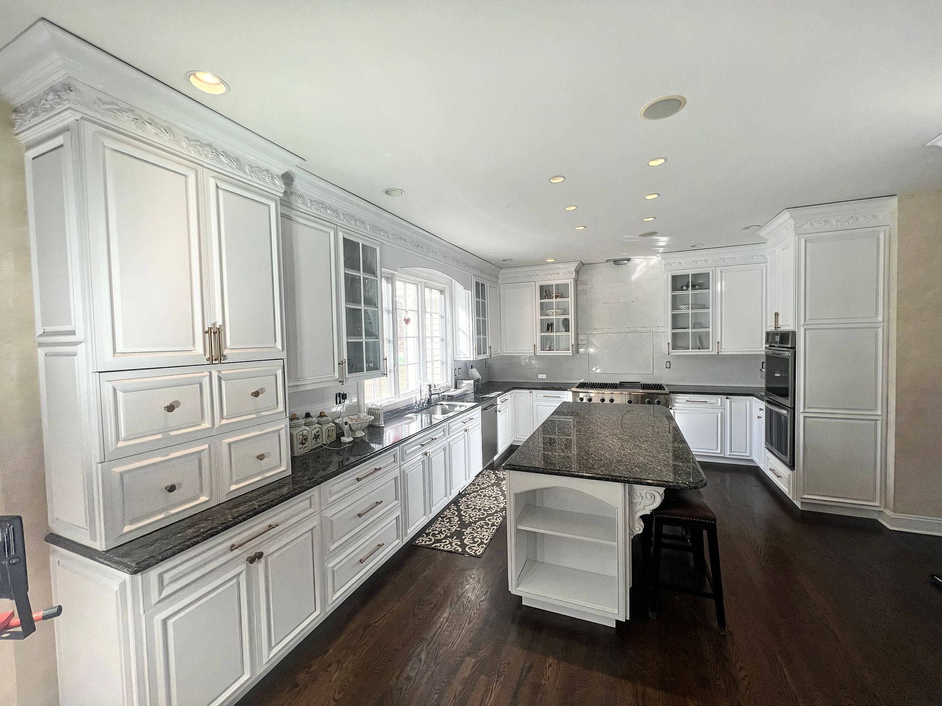 White kitchen with granite countertops, island, cabinets, and dark wood floors.