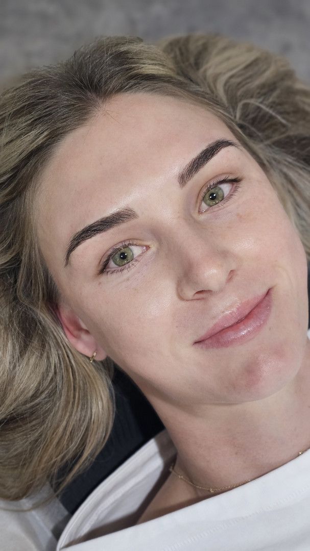 Close-up portrait of a person lying down, with wavy hair and a soft smile on a gray surface — On Point Cosmetic Tattoo Studio In Buderim, QLD