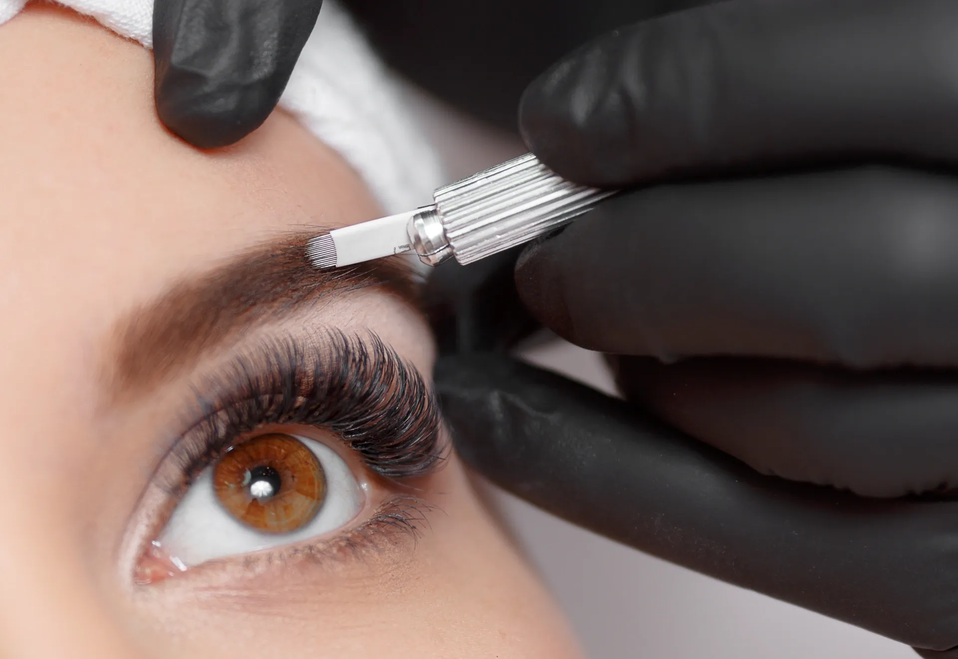 Person Receiving Microblading on an Eyebrow; Black Gloved Hand Holding a Tool — On Point Cosmetic Tattoo Studio In Caloundra, QLD