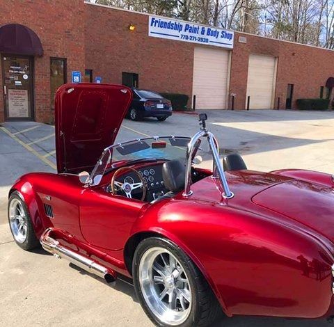 Red sports car with open hood parked outside a strip mall in front of a sign for Friendship Paint & Body Shop