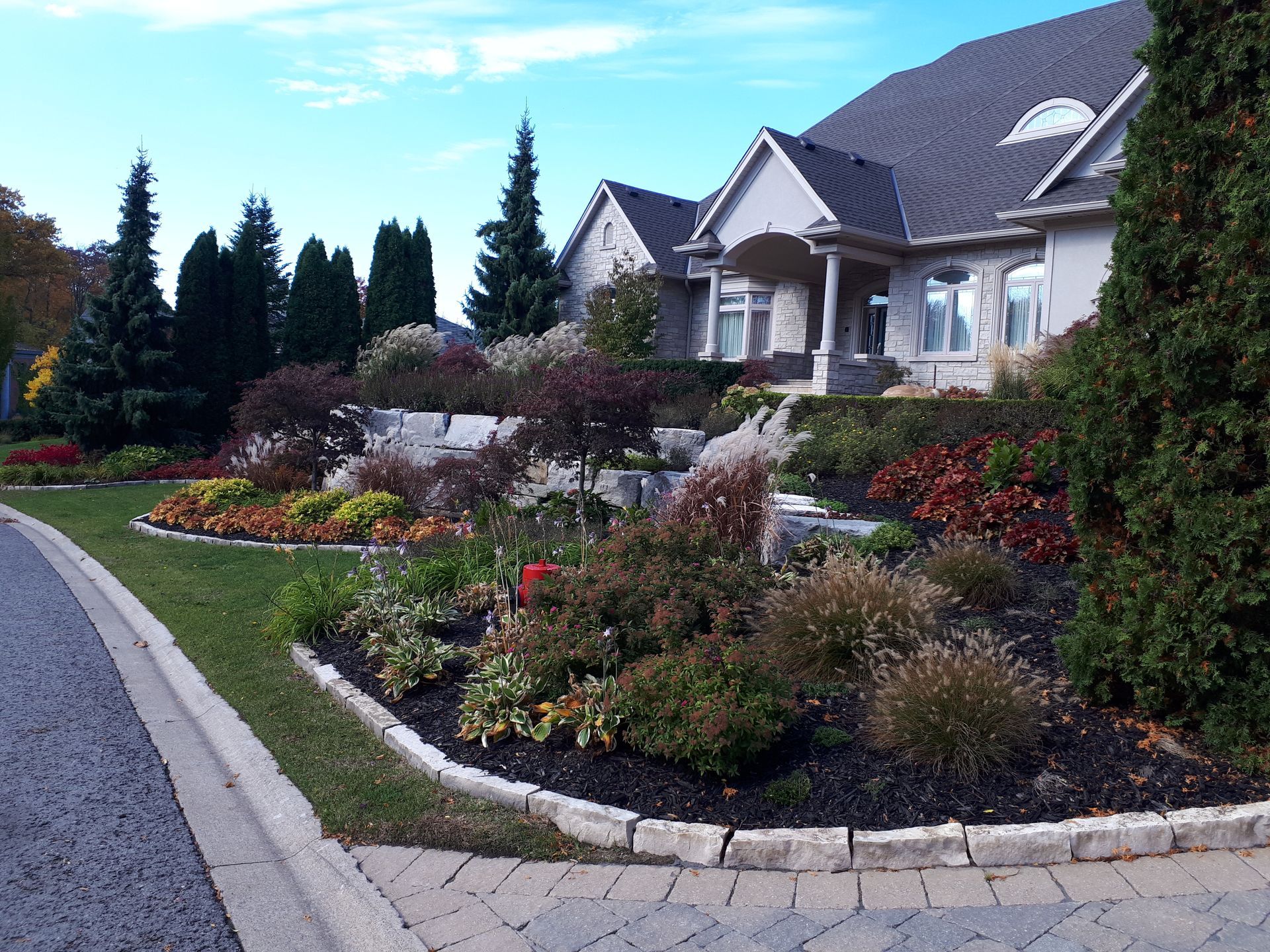 A large suburban home featuring a landscaped front yard with stone retaining walls, colorful shrubs, and mulch beds.
