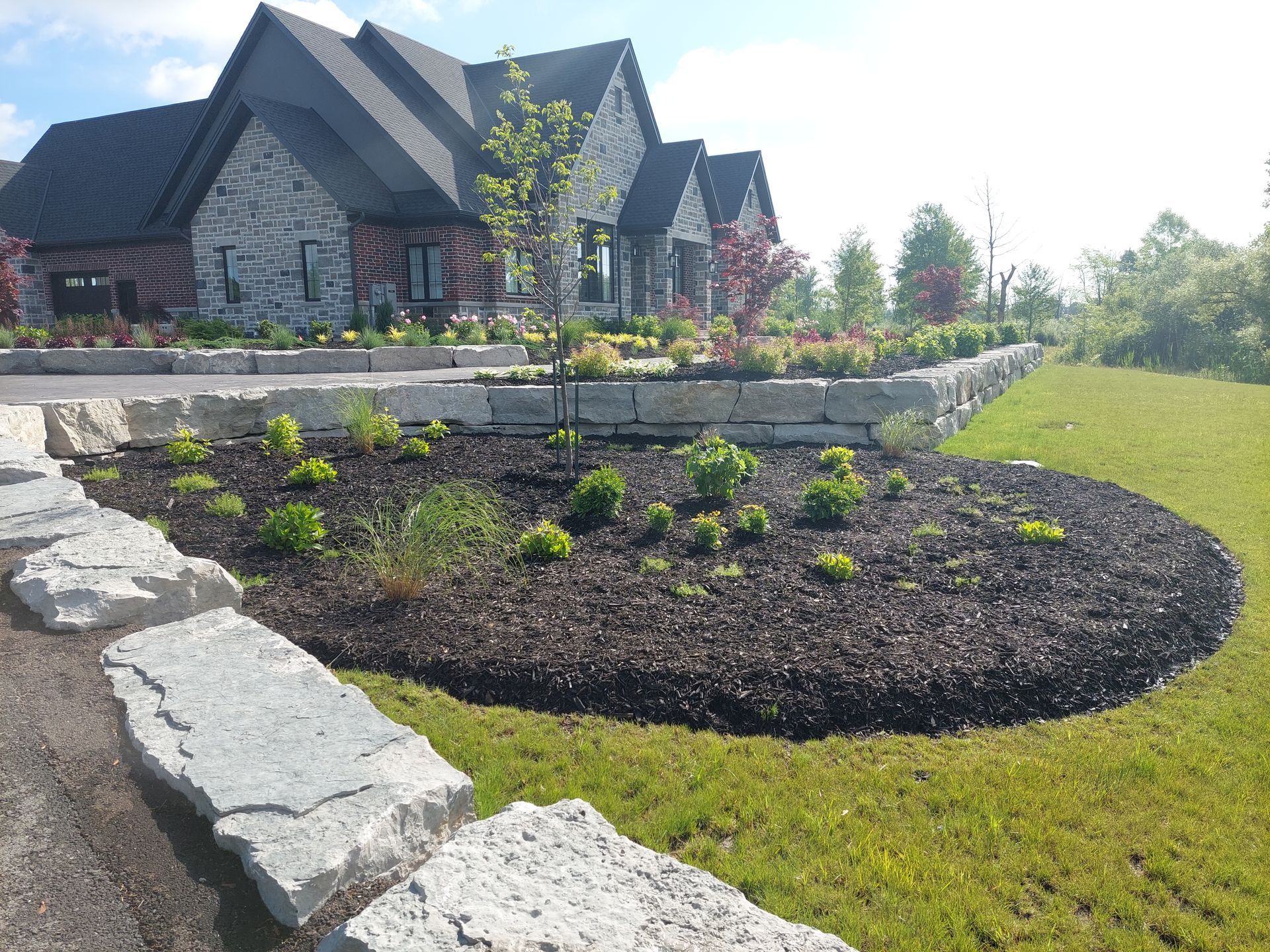 A suburban home with a stone facade, featuring tiered landscaping with large limestone retaining walls and dark mulch.
