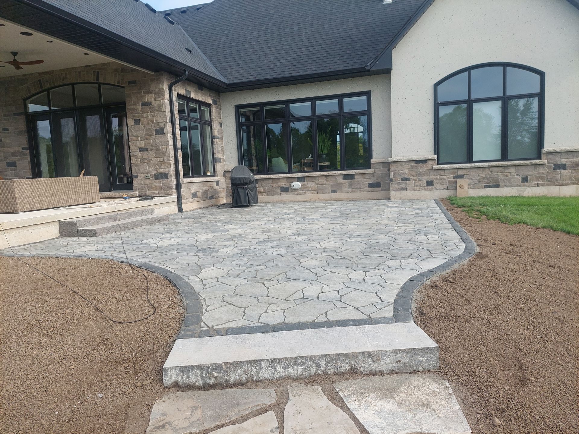 A light-colored stone patio with a decorative border and a single wide step, set against the back of a house.