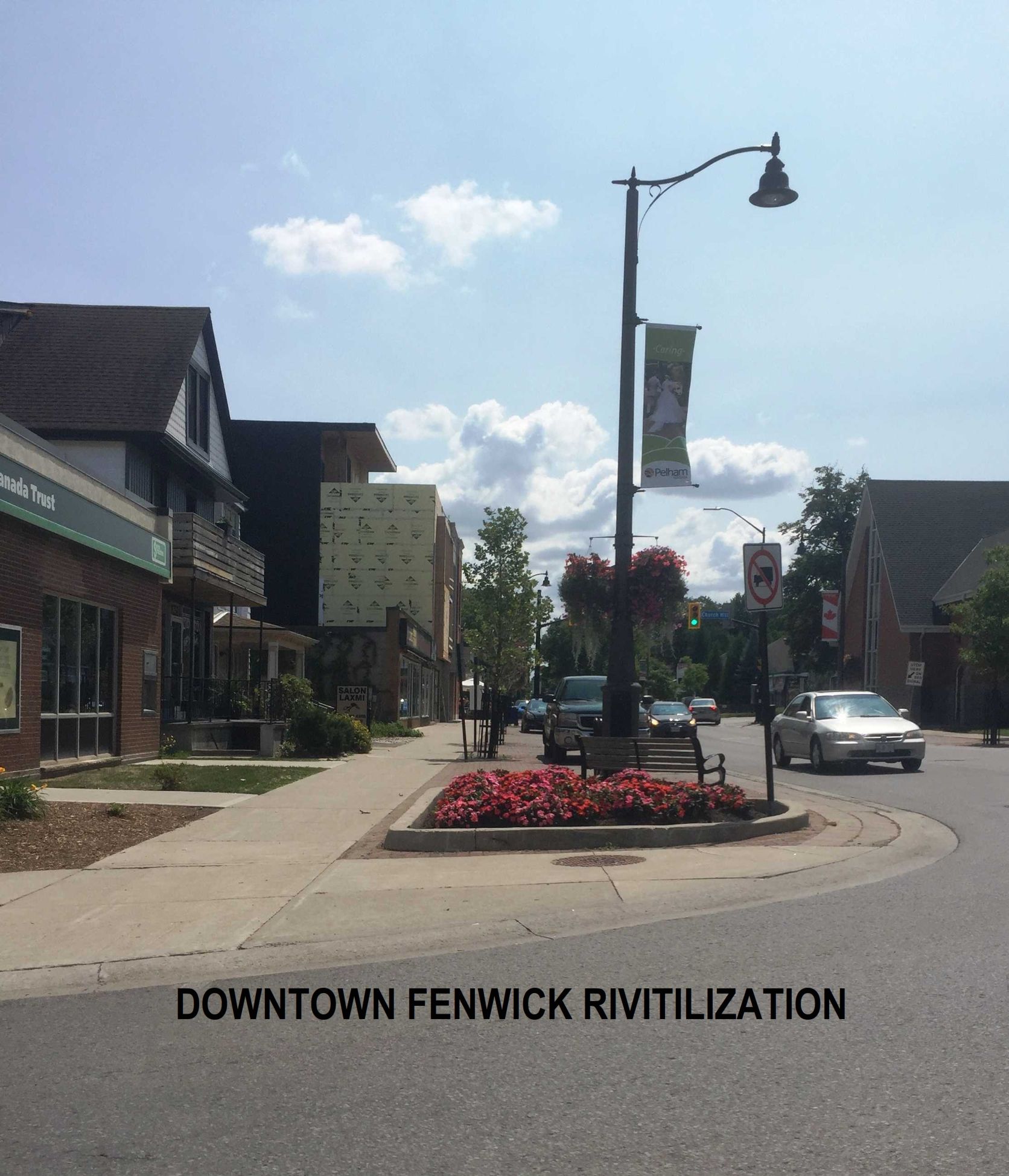 A street view of Downtown Fenwick, featuring a sidewalk, landscaped flower bed, street lamp, and passing cars.