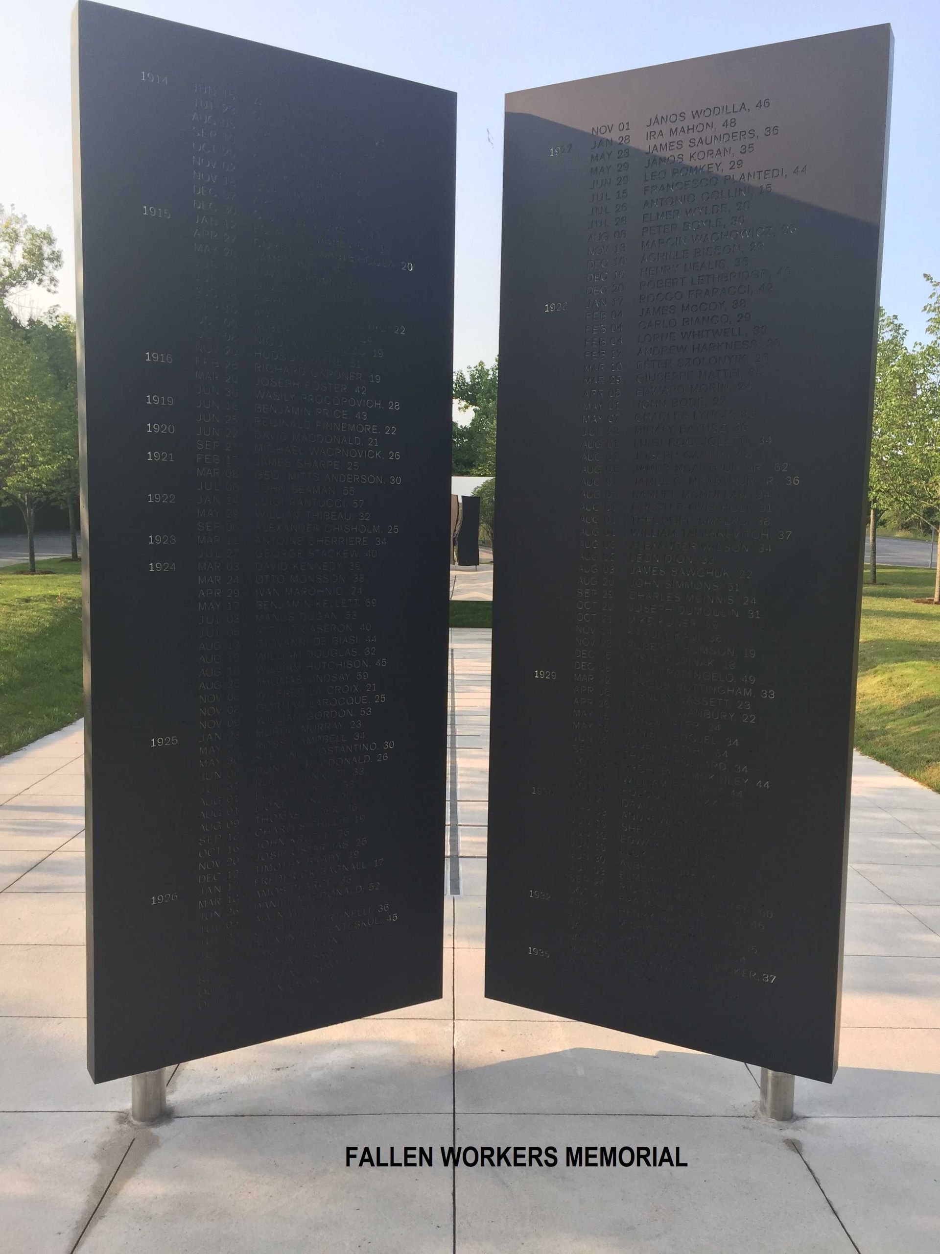 Two upright, dark-colored memorial slabs etched with names, set in an outdoor area labeled Fallen Workers Memorial.