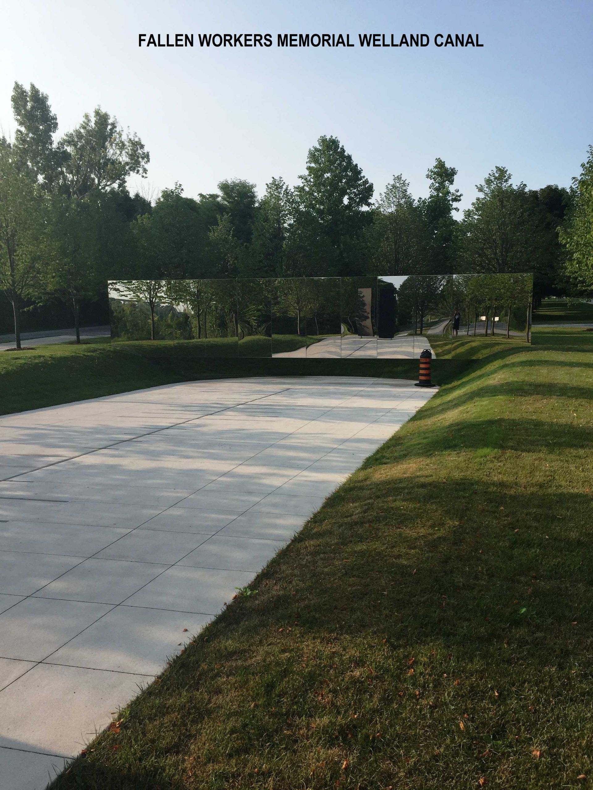 Fallen Workers Memorial at the Welland Canal, featuring a paved path leading to a reflective monument among green trees.