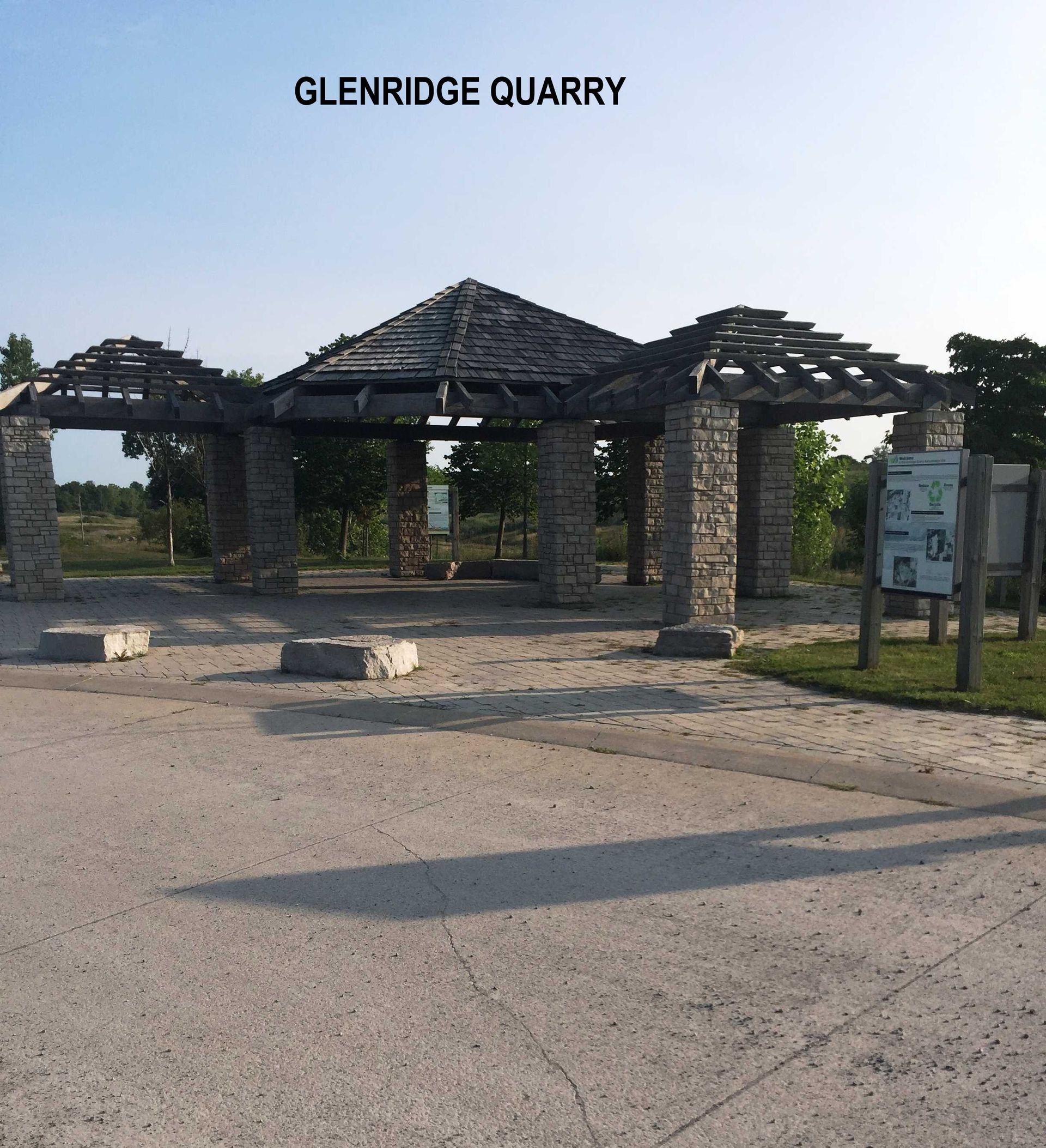 An outdoor stone gazebo structure at Glenridge Quarry with a wooden pergola roof, set in a gravel area under a clear sky.
