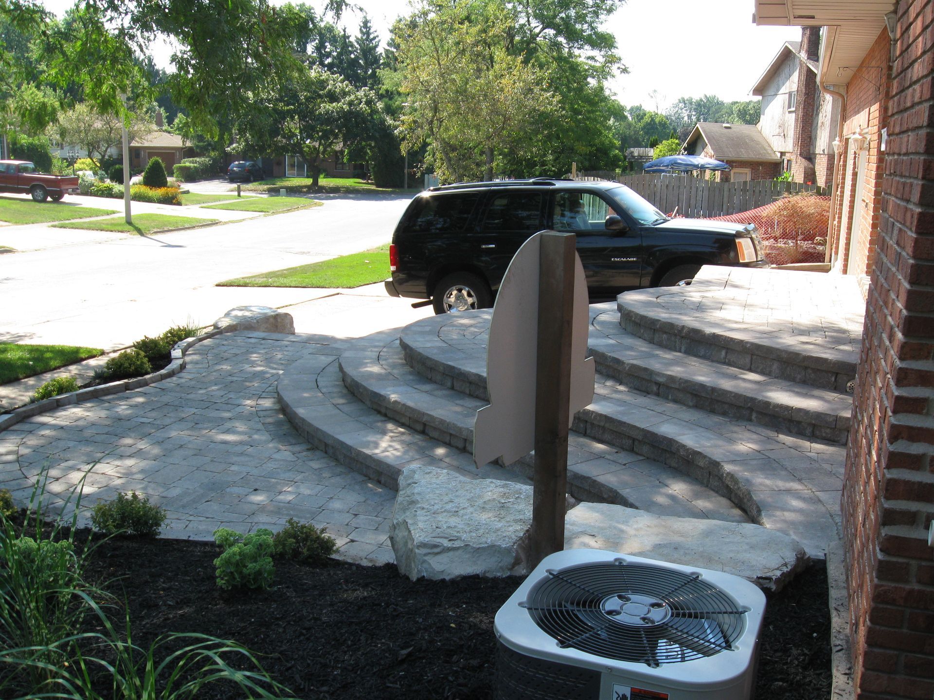 A newly installed curved paver patio and tiered steps leading to a brick house, with a black SUV parked in the driveway.