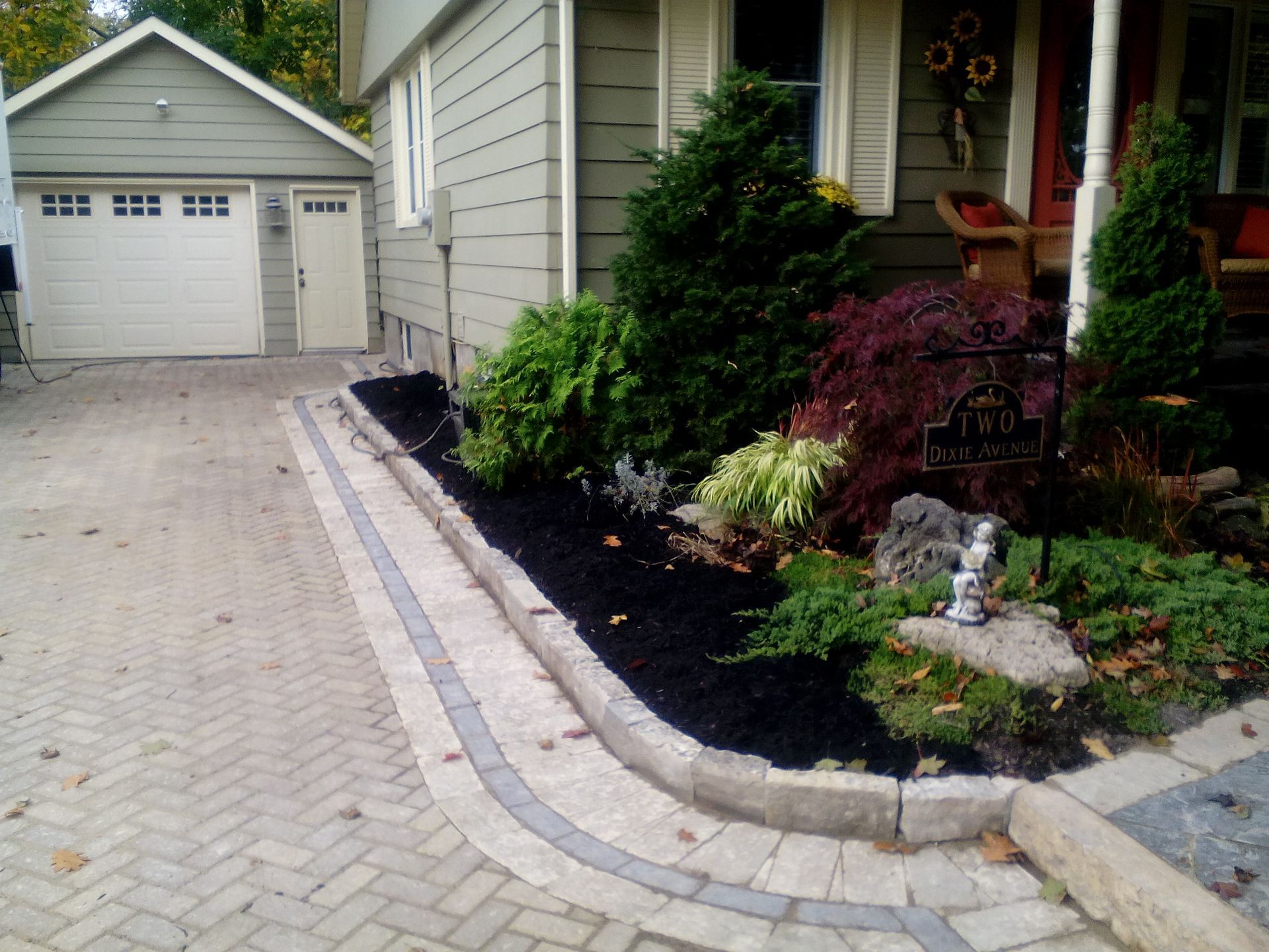 A paved driveway leading to a garage next to a house with a landscaped garden bed containing mulch and small shrubs.