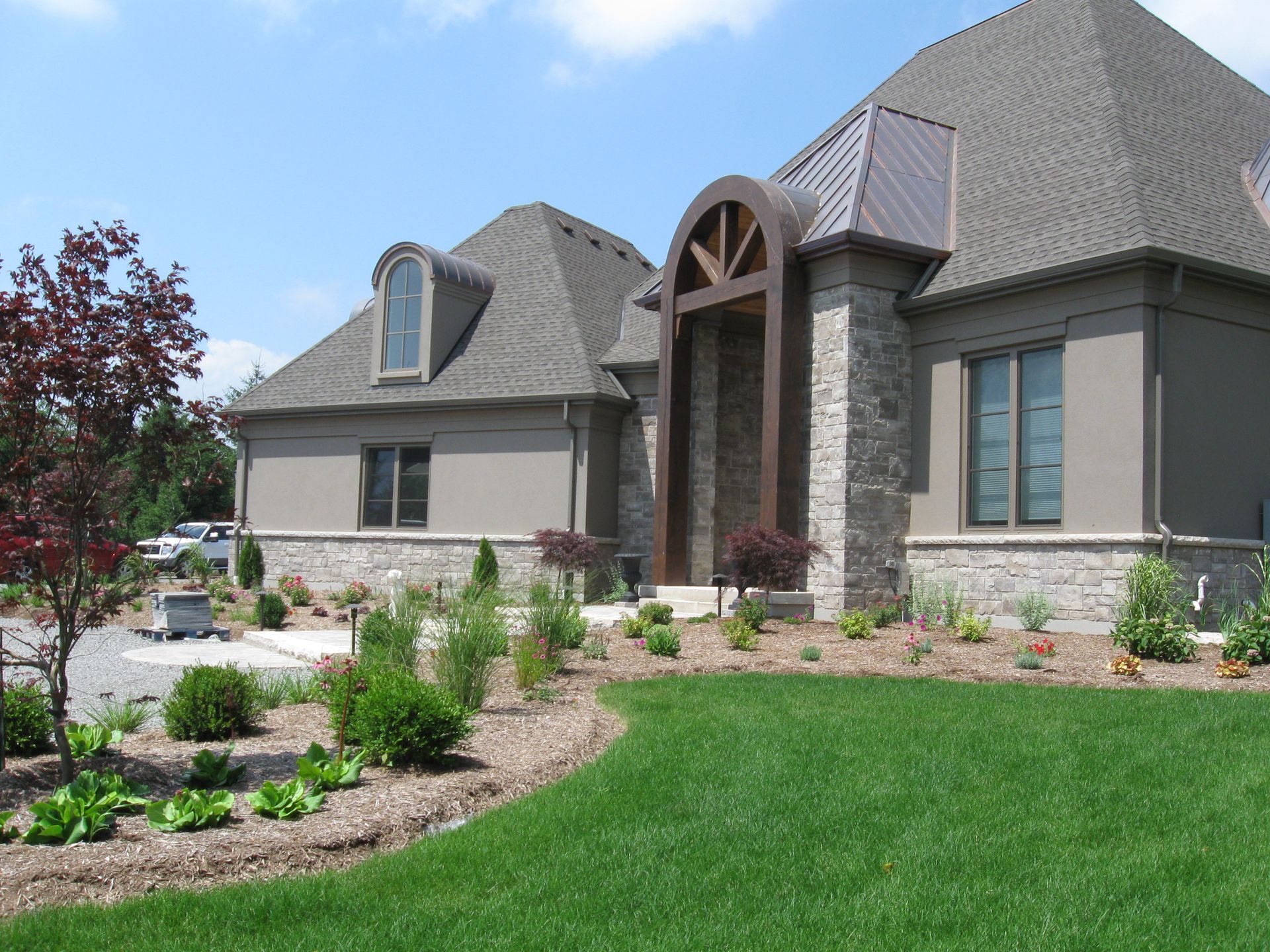 A single-story suburban home with a stone and stucco facade, an arched entryway, and landscaped front lawn under blue skies.