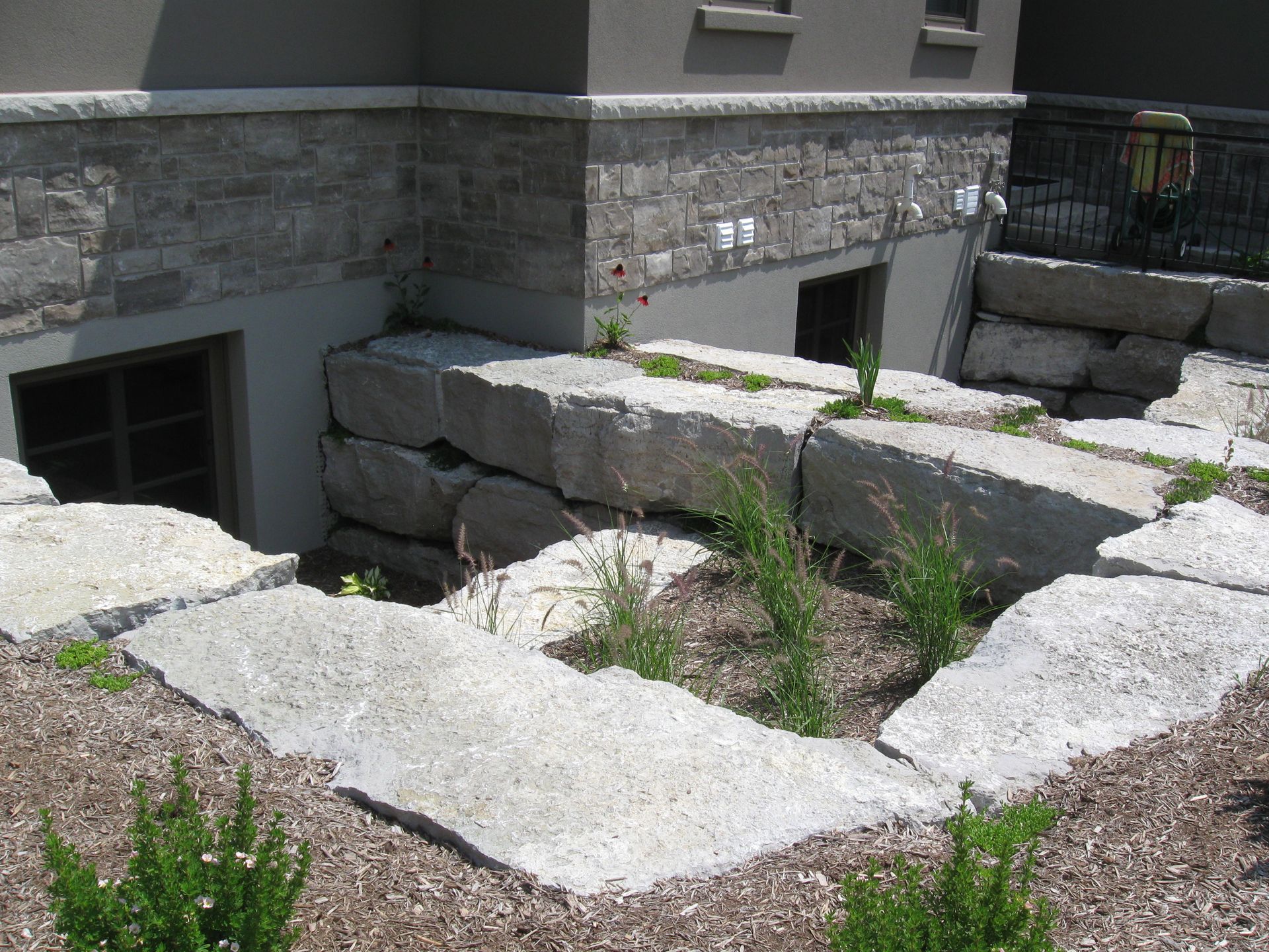 A light-colored stone window well provides egress for a house with gray stone foundation walls.