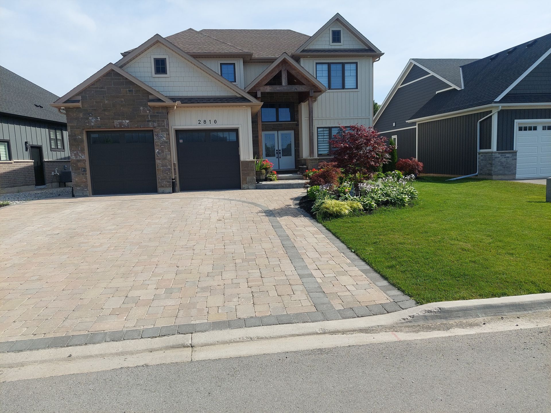 A two-story suburban home with a stone and light-colored siding exterior, a paver driveway, and a landscaped front yard.