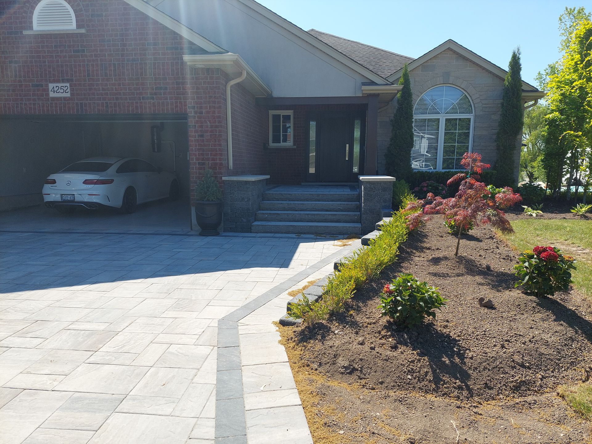 A single-story suburban house with brick and stone siding, a two-car garage containing a white car, and a paved driveway.