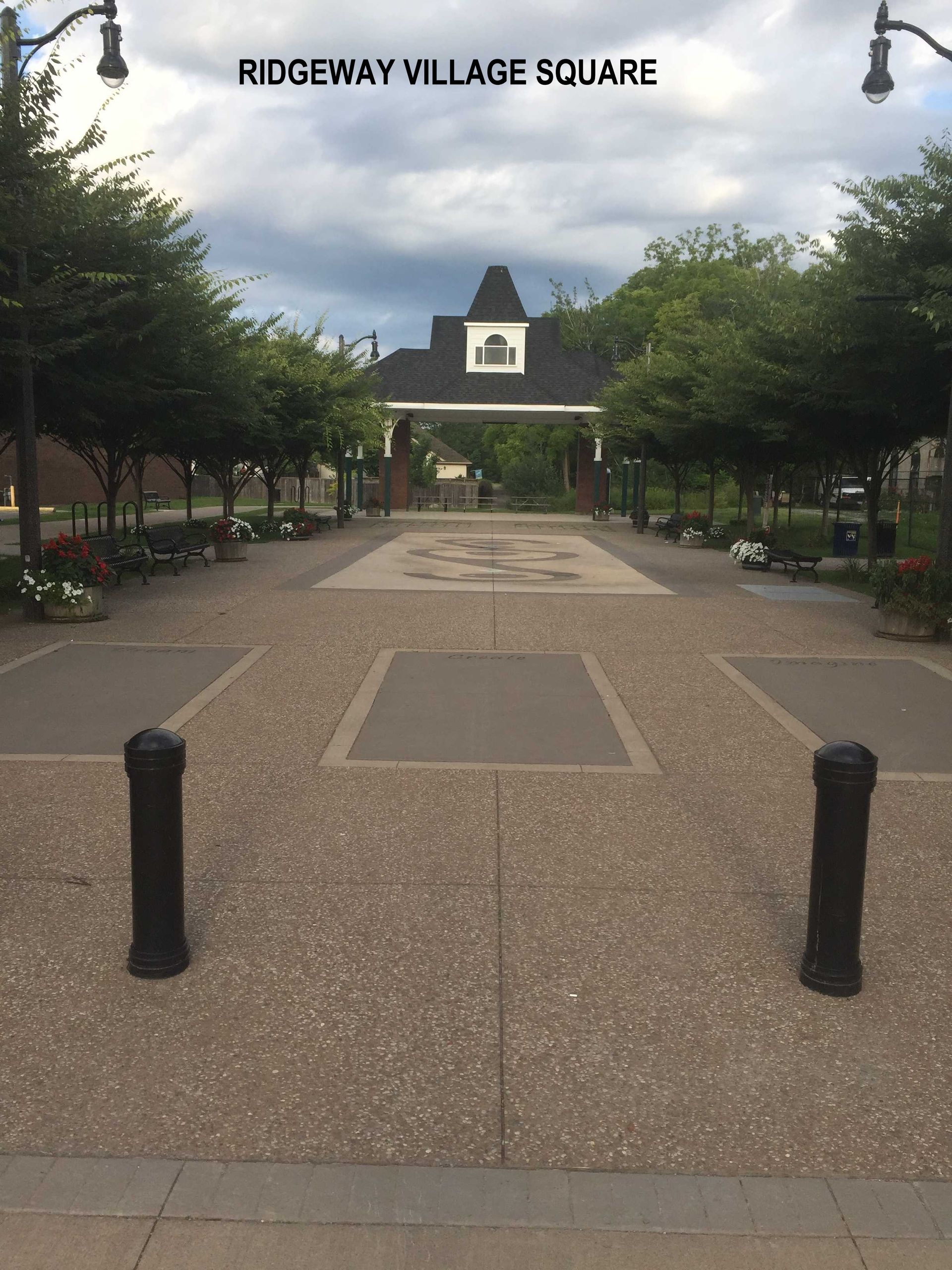Ridgeway Village Square with a tree-lined stone path leading to a covered structure under a cloudy sky.