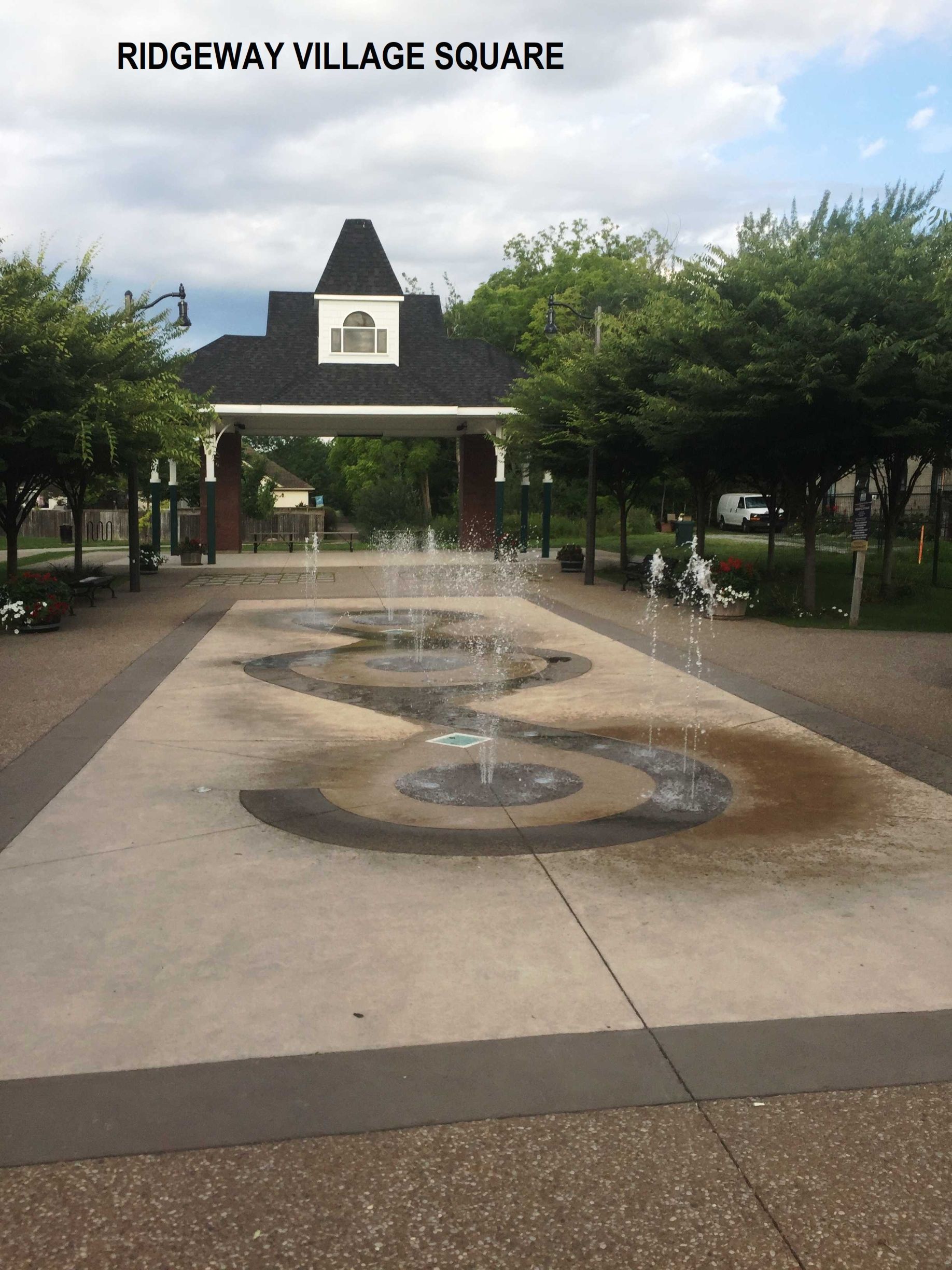 Ridgeway Village Square with a multi-jet water feature in a paved plaza leading toward a covered pavilion.