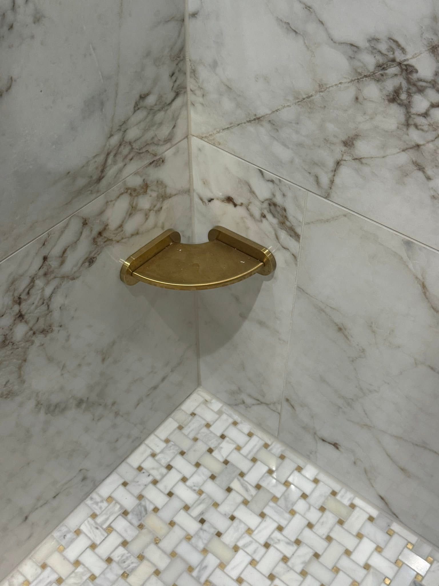 A shower with a corner shelf and a marble wall.