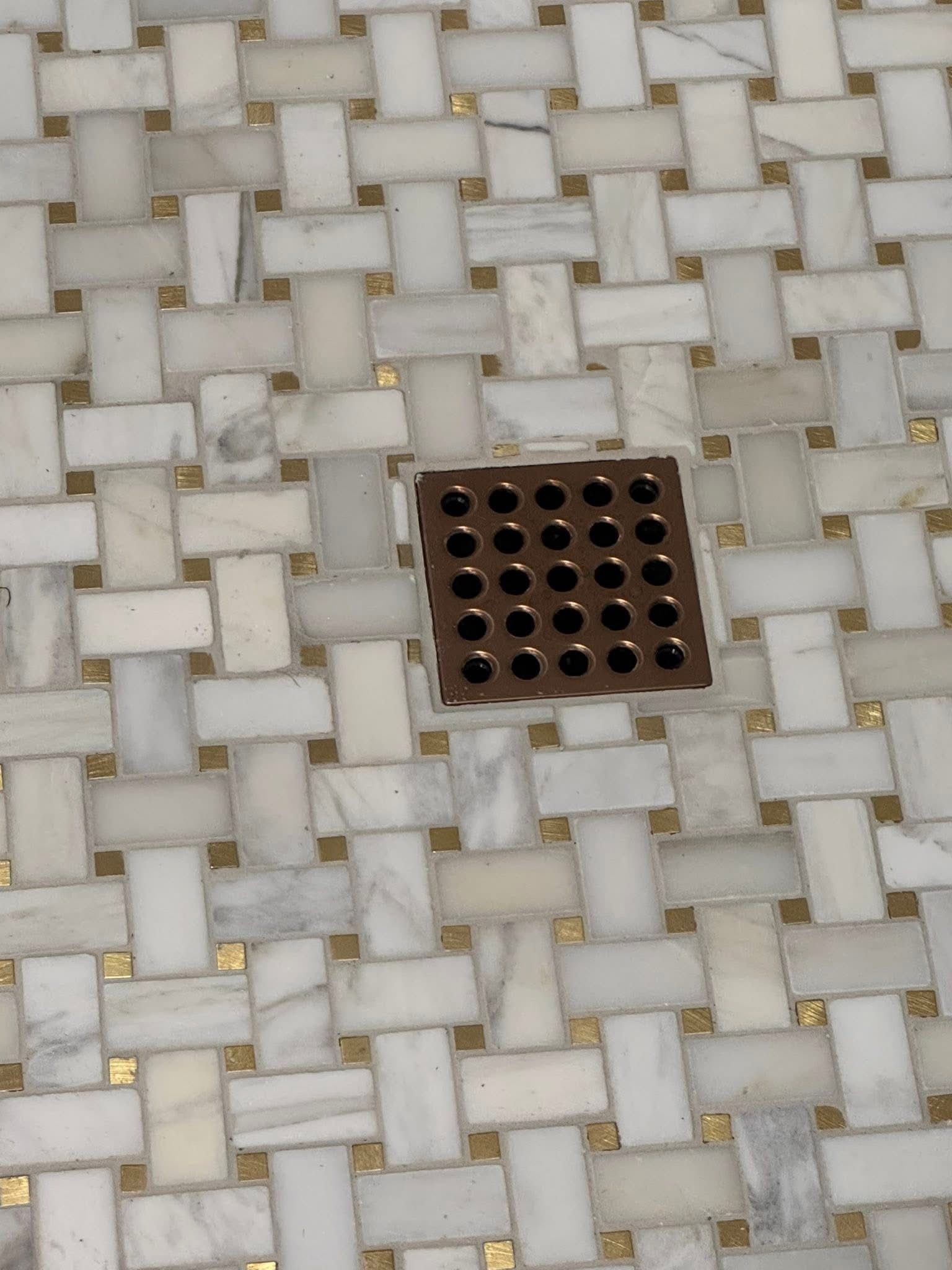 A drain on a marble floor that looks like a basket weave