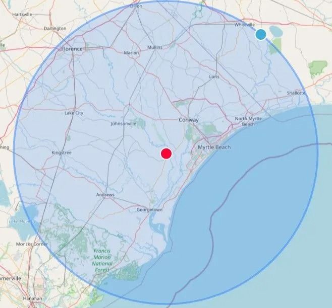 Map with blue shaded circular area and two location markers near the coast, one red and one blue-green