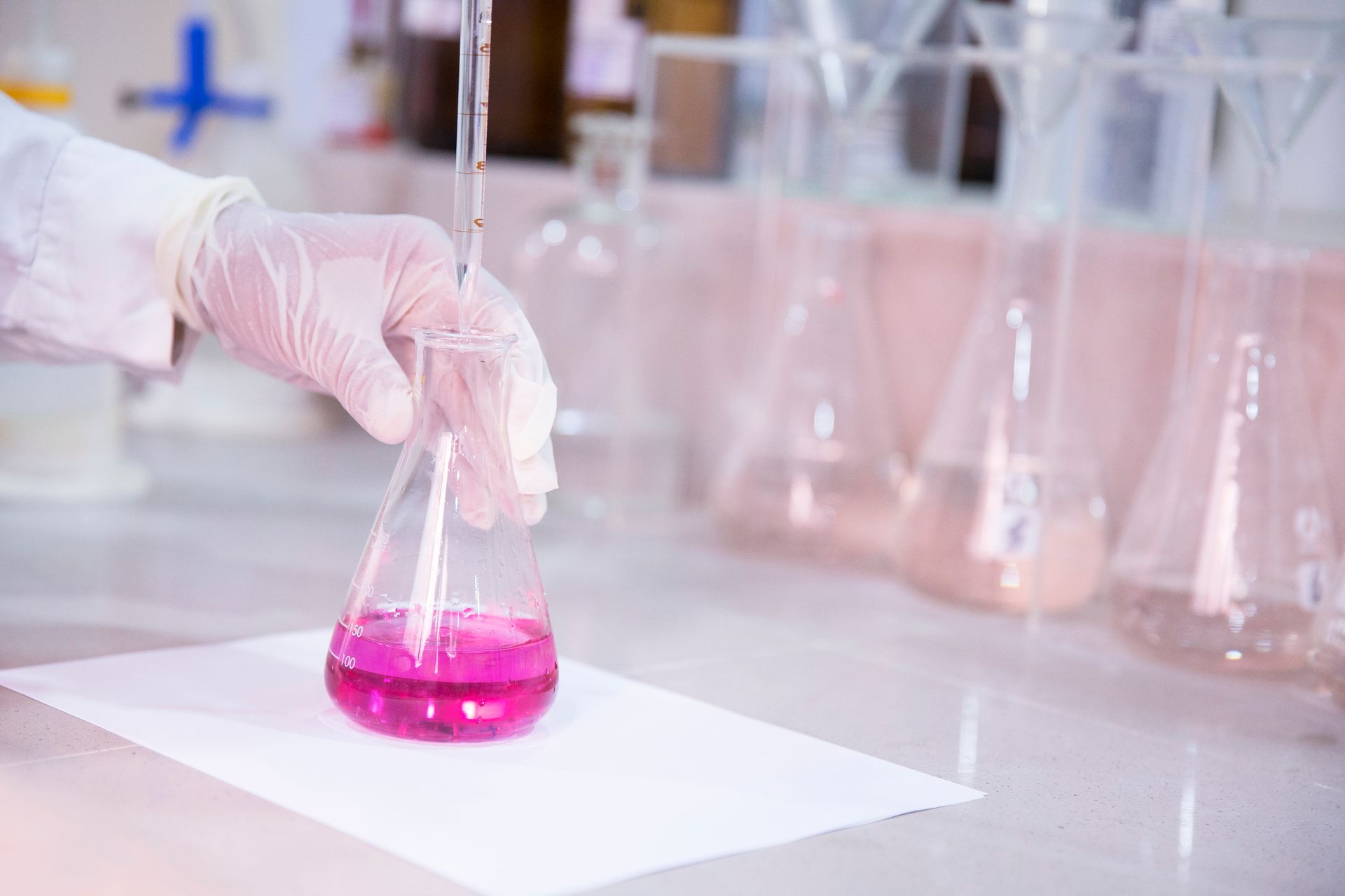 Gloved hand holding a flask with bright pink liquid in a lab setting