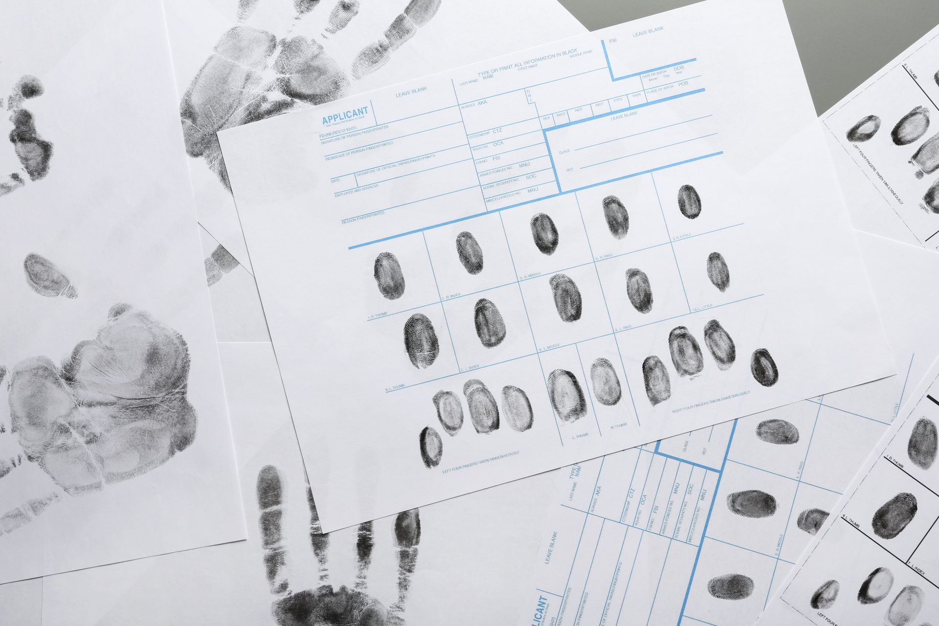 Fingerprint analysis sheets with multiple prints and handwritten notes on a white desk
