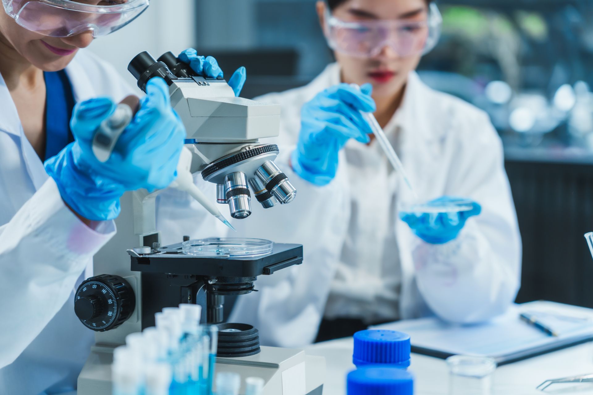 Scientists in lab coats using a microscope with blue gloves in a laboratory