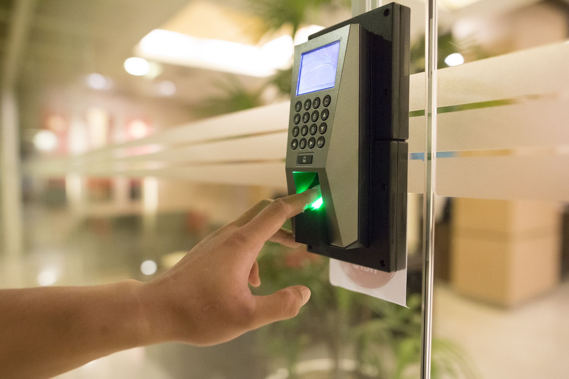 Hand pressing a green-lit fingerprint scanner on a wall-mounted access control keypad
