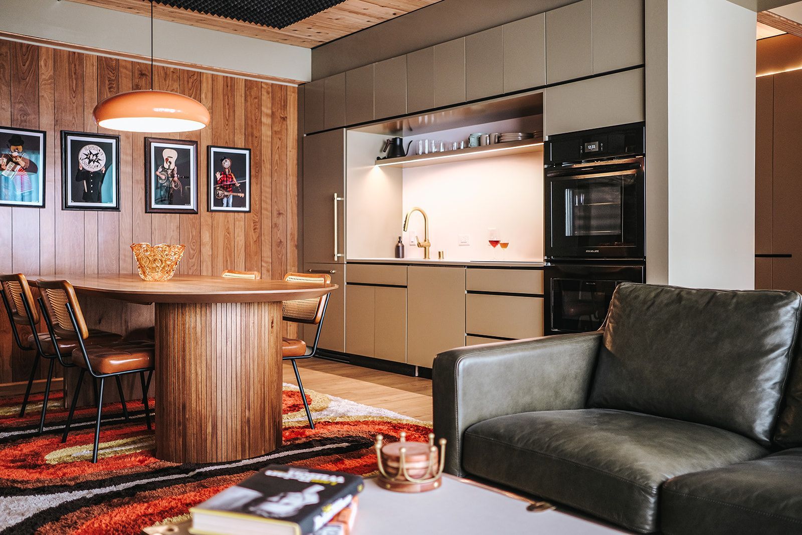 Modern kitchen and dining area with wood paneling, round table, leather chair, and black sofa