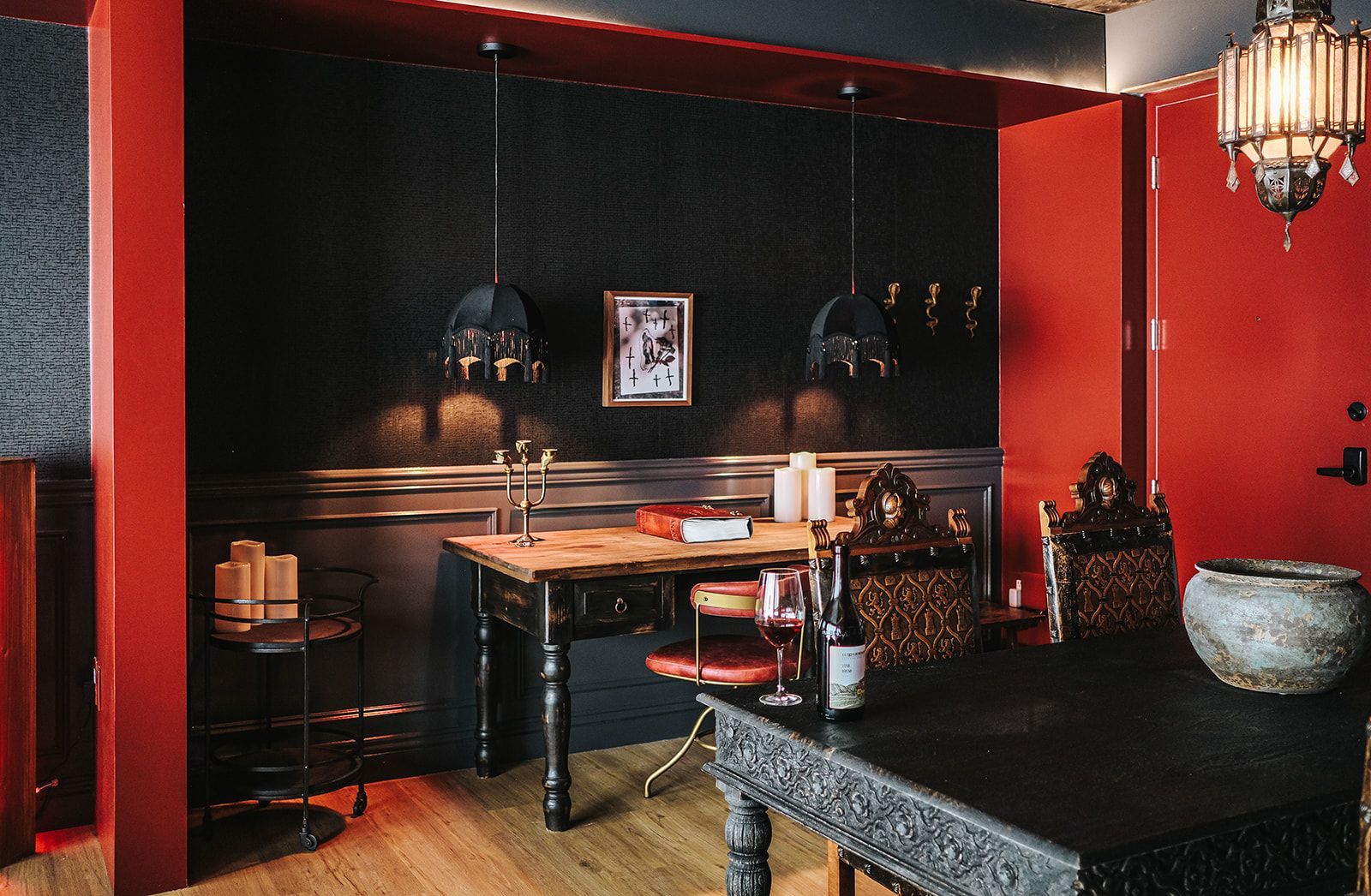 Dim red-and-black dining room with a small table, chairs, and ornate decor.