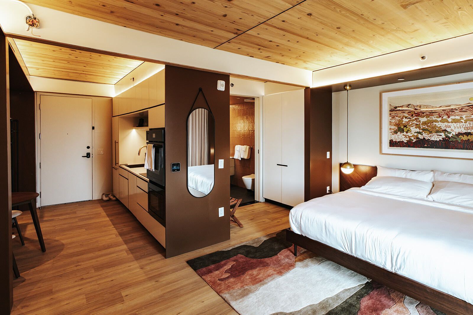 Modern bedroom with bed, wood ceiling, colorful rug, and large city-view window