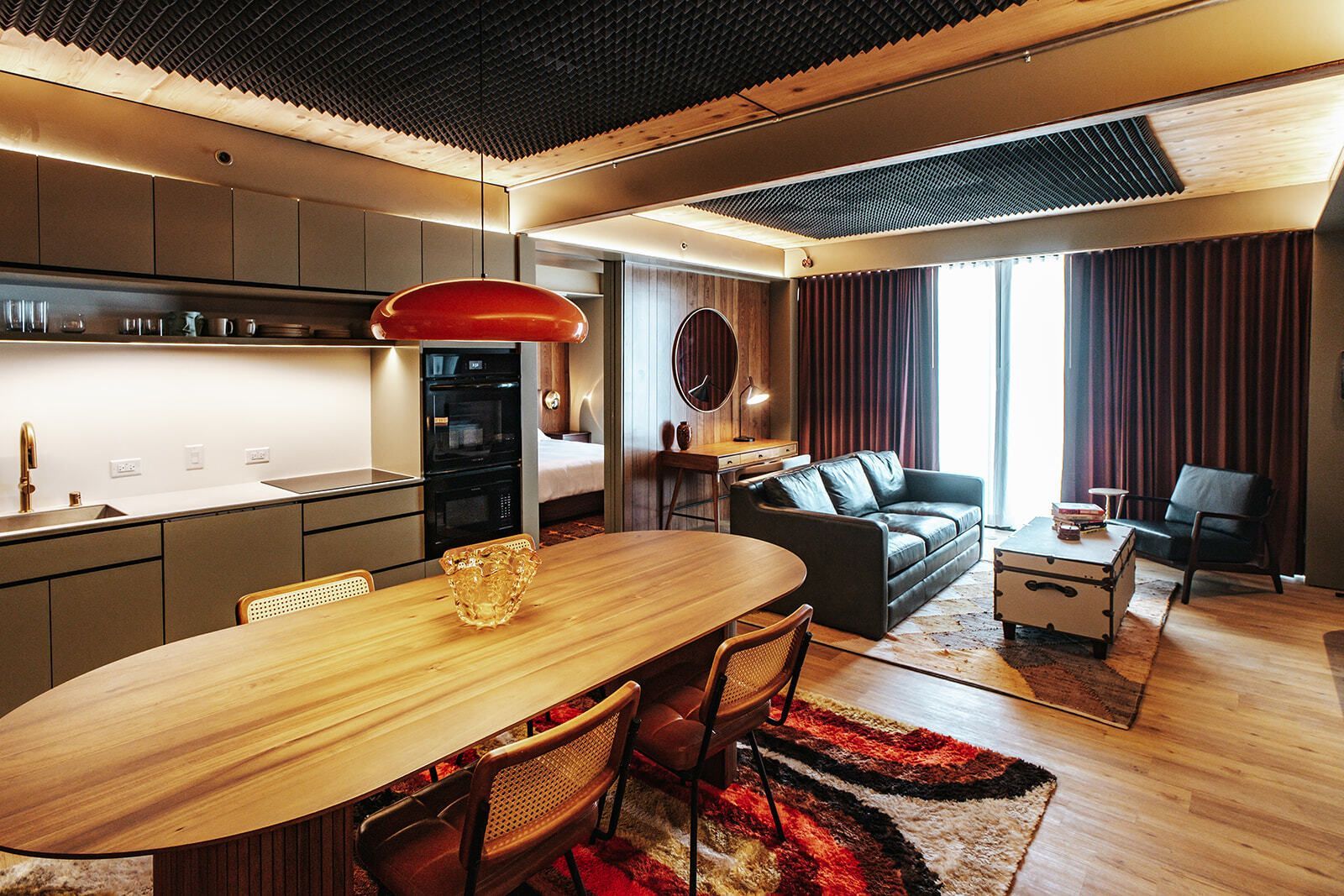 Modern kitchen and dining area with wood paneling, round table, leather chair, and black sofa