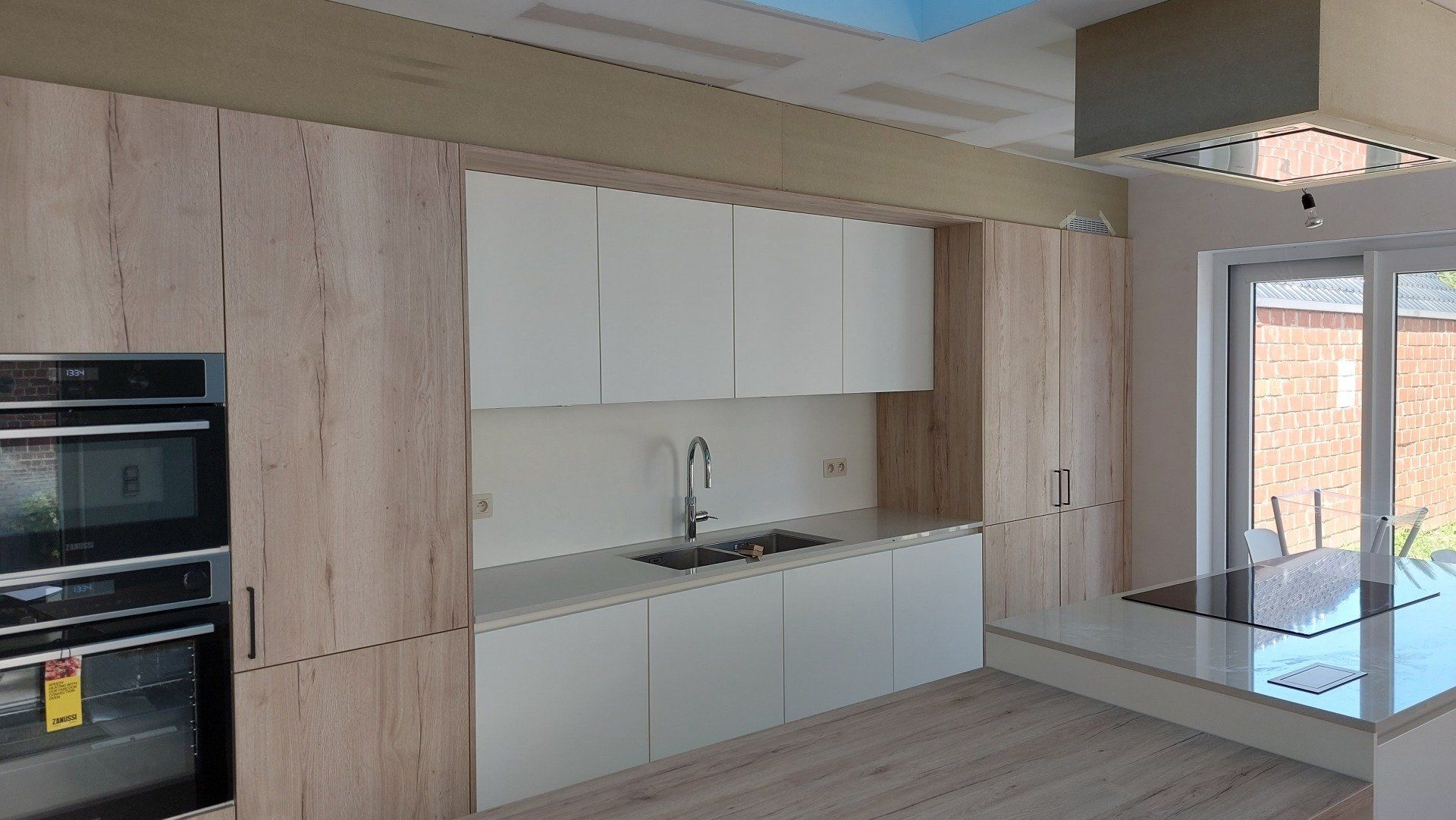 Moderne keuken met licht hout, witte kasten, roestvrijstalen apparatuur en een kookeiland met marmeren blad.