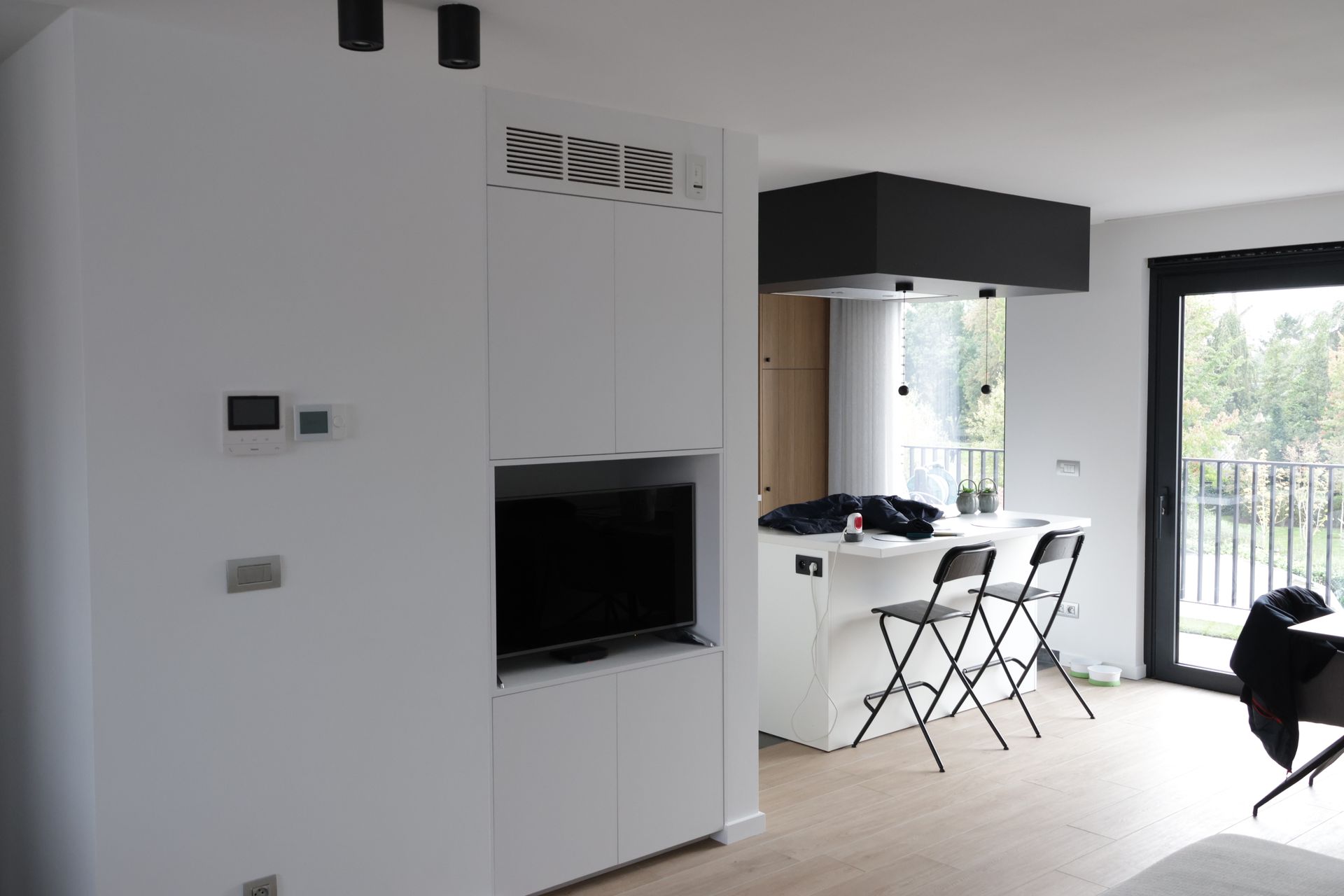 Modern wit interieur met een ingebouwde tv, aanrecht en zwarte accenten. Op de achtergrond is een raam met een balkon.