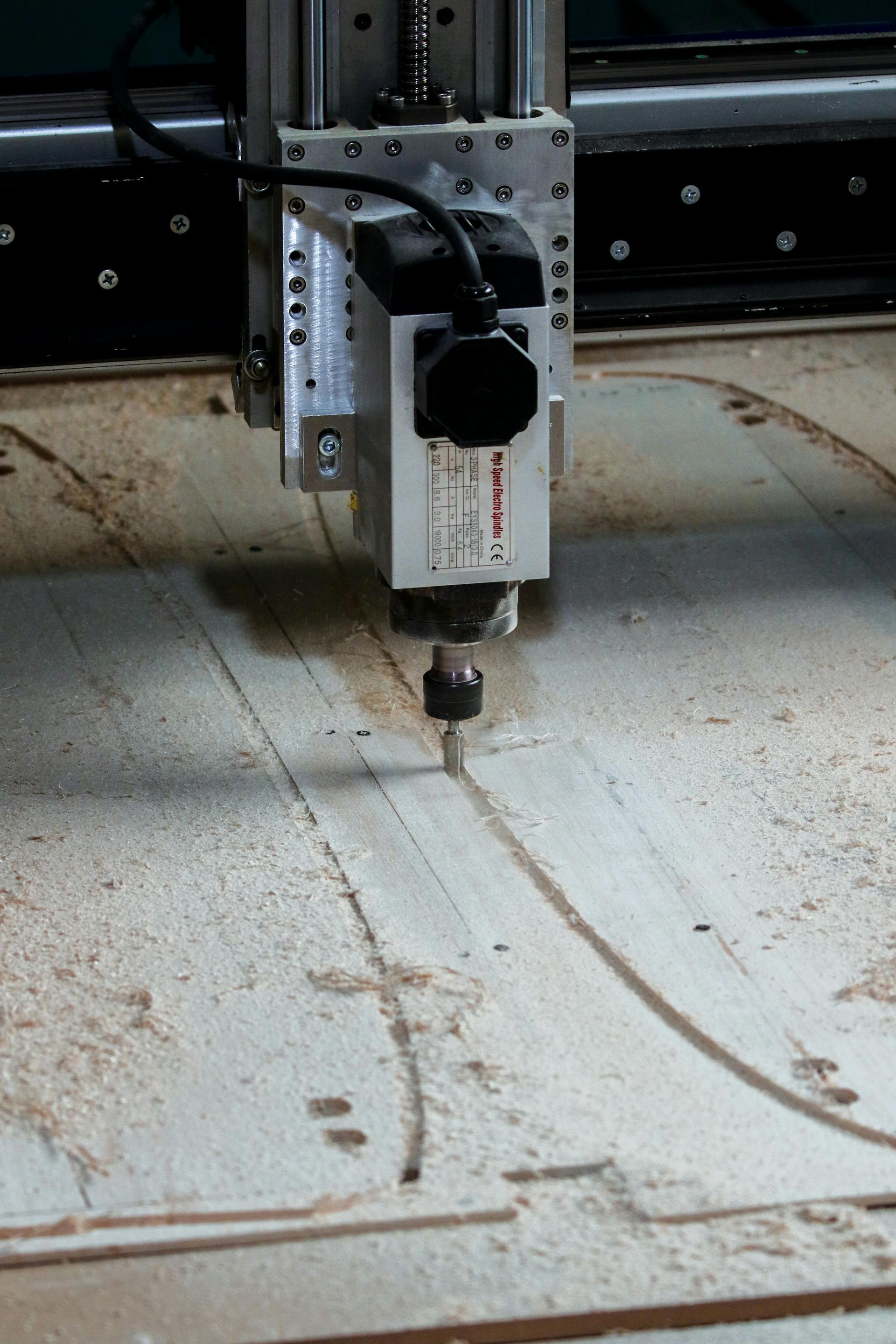 CNC-machine snijdt een houten paneel, creëert gebogen lijnen en verwijdert zaagsel.