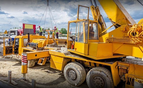 Yellow crane lifting a load at a construction site; workers in vests, cloudy sky.