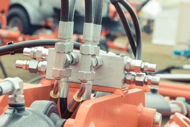 Hydraulic system on orange machinery with black hoses and silver connectors.
