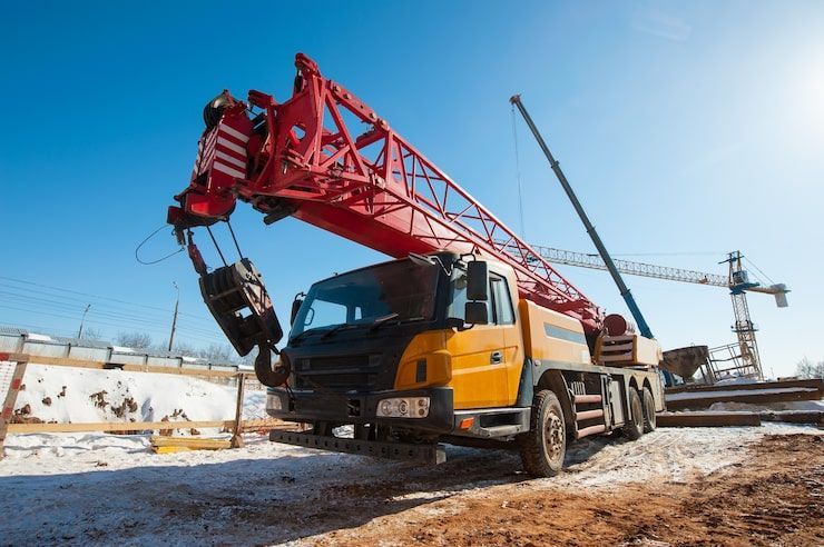 Yellow and red crane truck at a construction site against a clear blue sky.