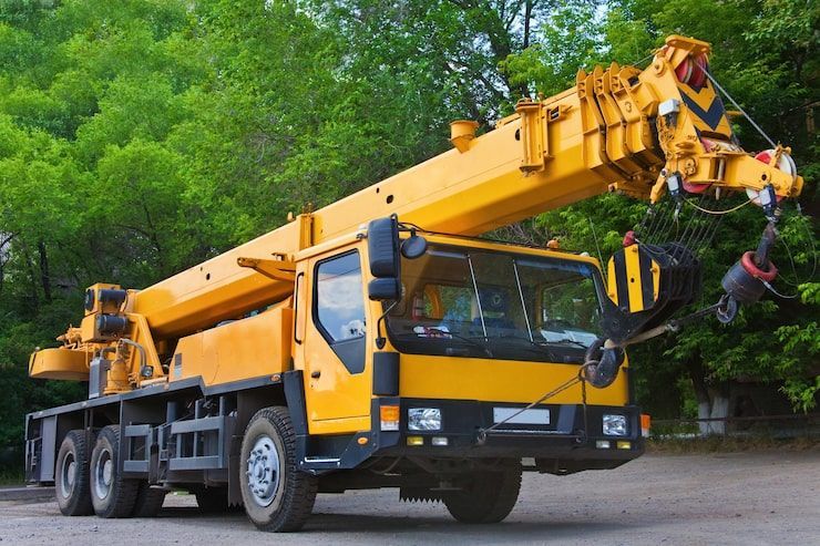 Yellow mobile crane on road with the boom extended, green trees in background.