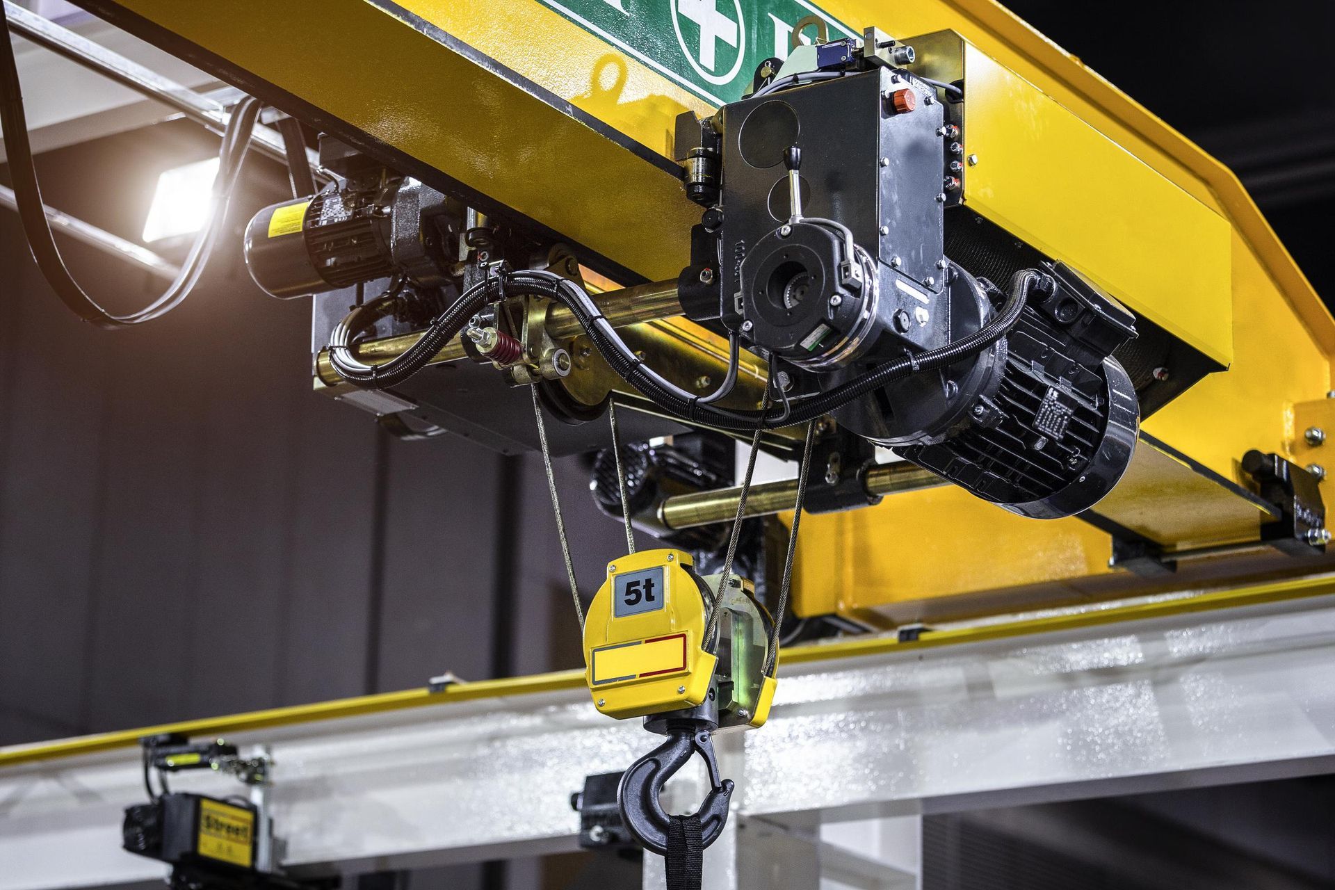 Yellow industrial overhead crane with black motors and a hook.