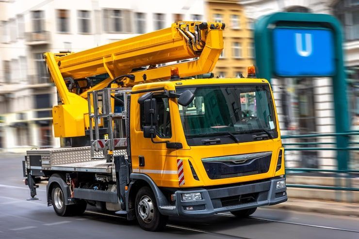 Yellow utility truck with crane boom on city street, near an