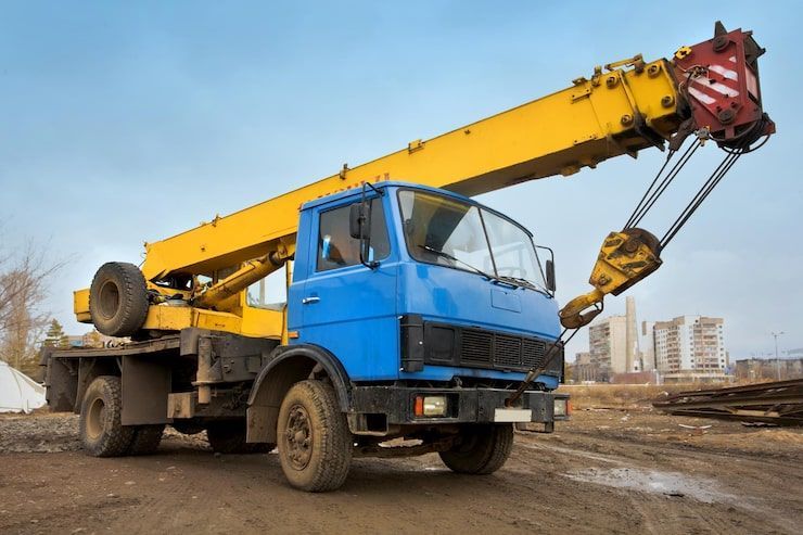 Blue and yellow crane truck on a construction site; the crane arm is extended upwards.