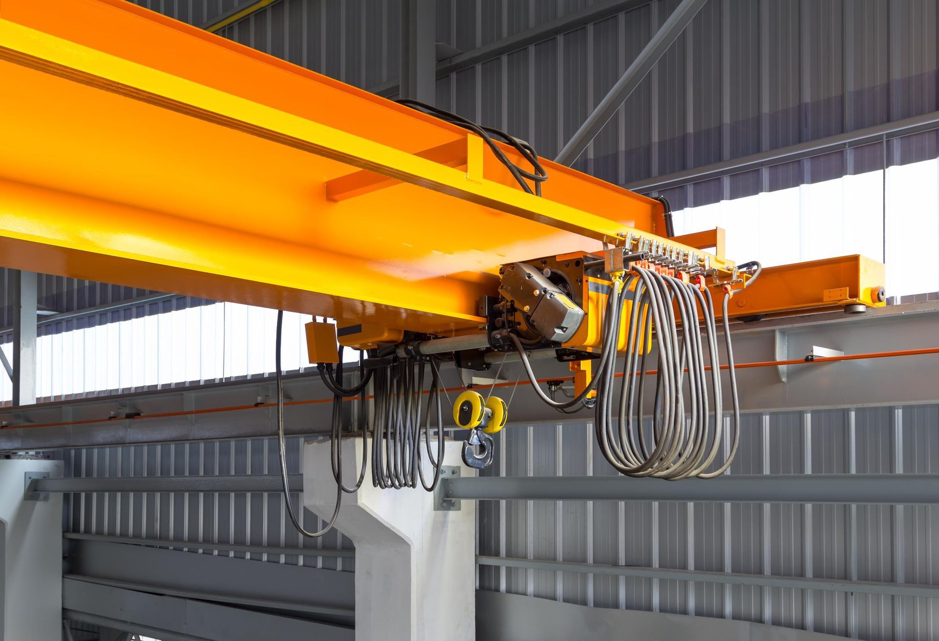 Yellow overhead crane in a factory setting, with exposed wiring and supports.