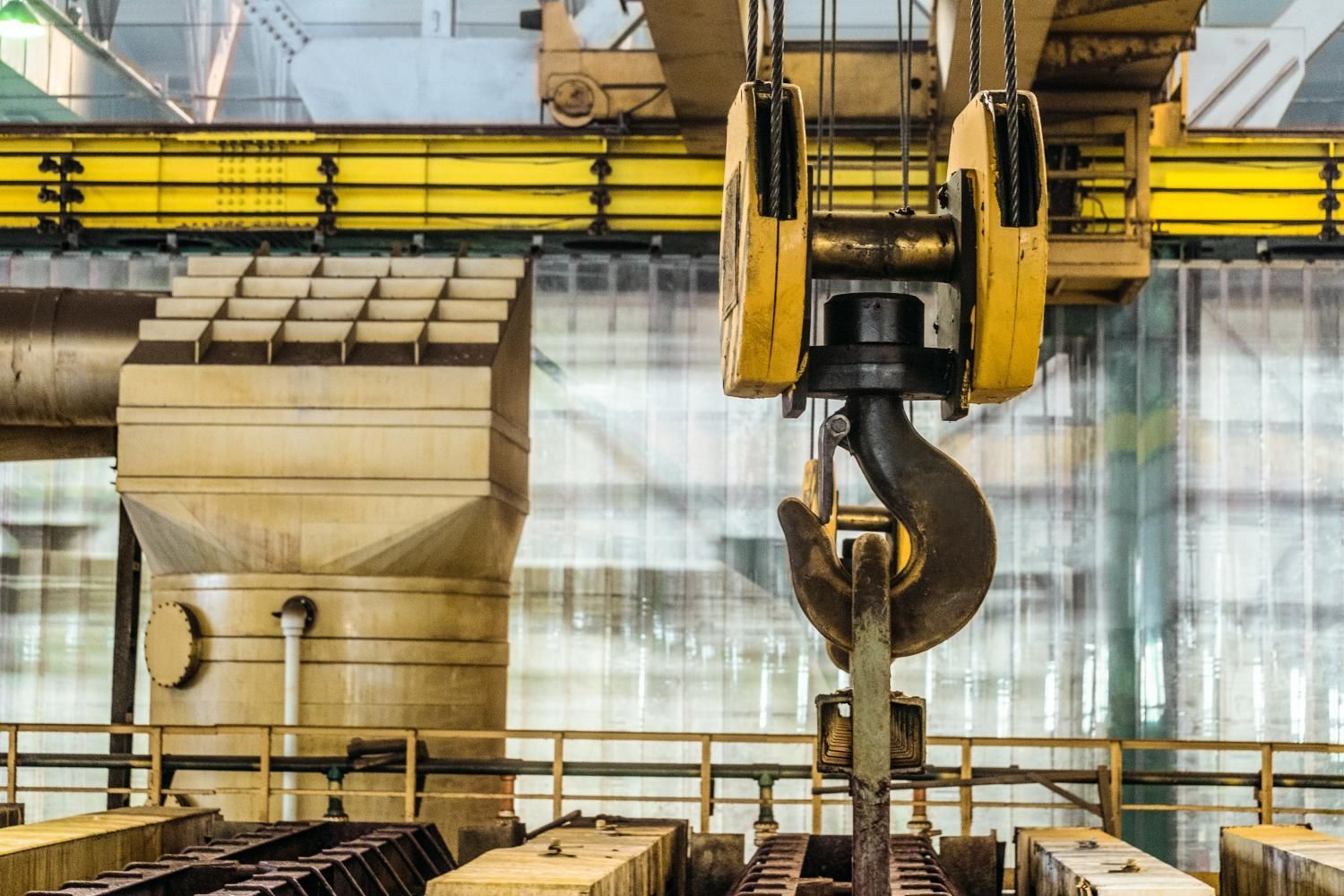 Yellow industrial crane hook in a factory setting.