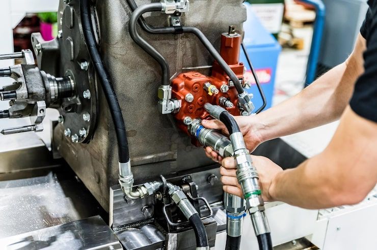 Person connecting hydraulic lines to a red pump on machinery.