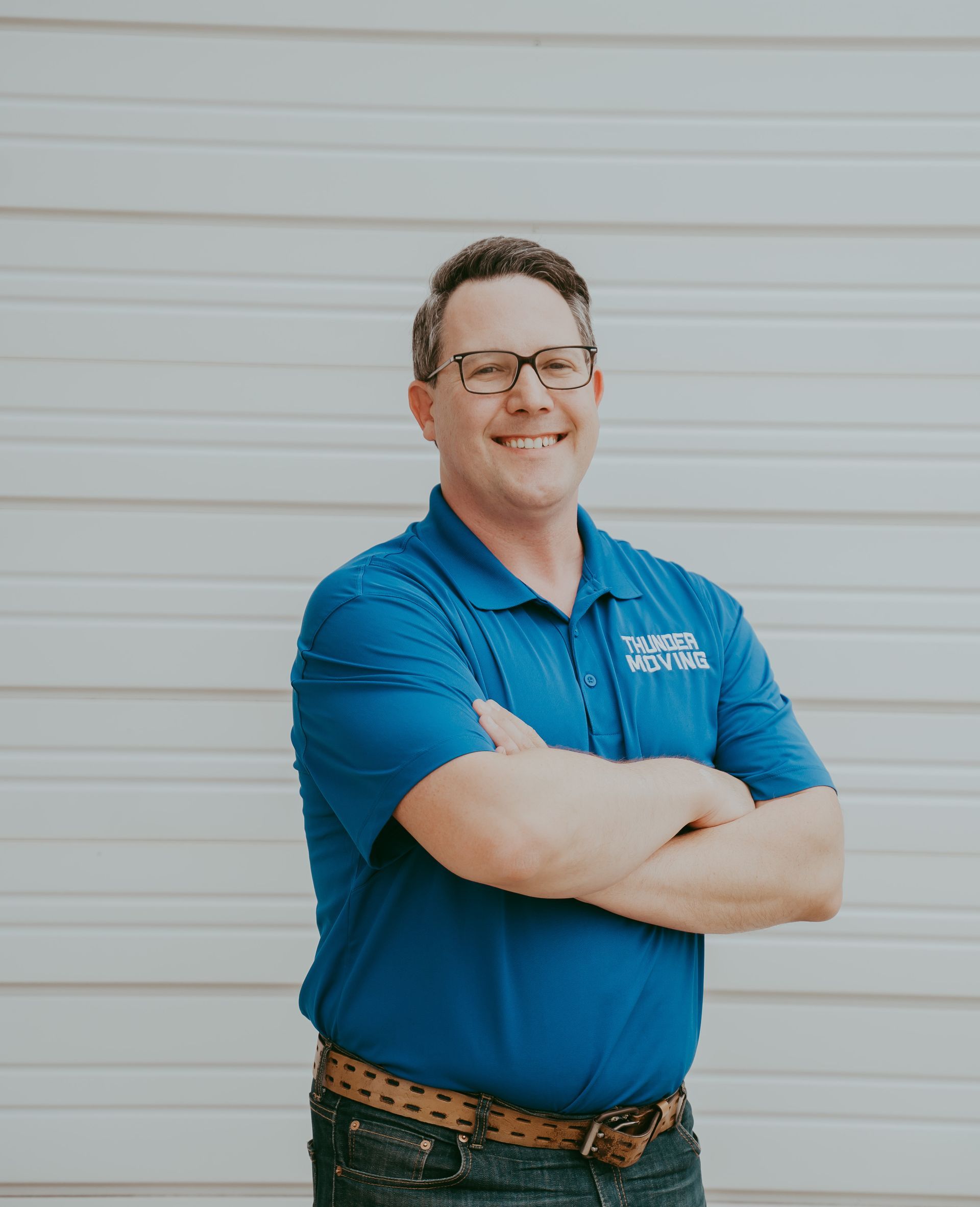 A man in a blue shirt is smiling and standing in front of a wall.