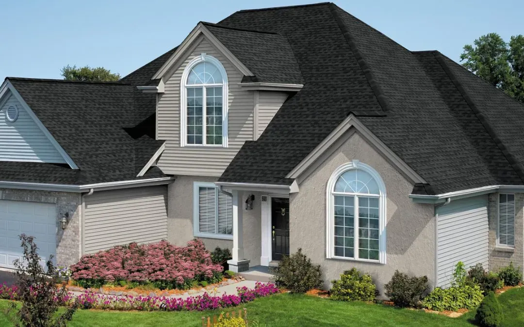Suburban house with gray siding, dark roof, arched windows, and a colorful flower bed in front