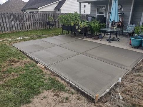 Newly poured concrete patio square divided into six sections, located in a backyard next to a house with patio furniture.