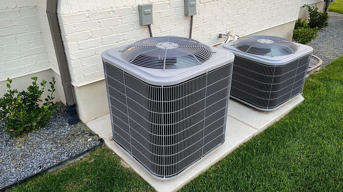 Two air conditioners are sitting on the side of a house.