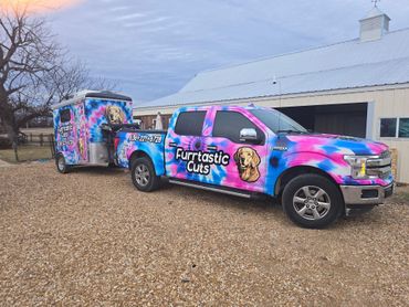 A pink and blue truck with a trailer attached to it is parked in front of a building.