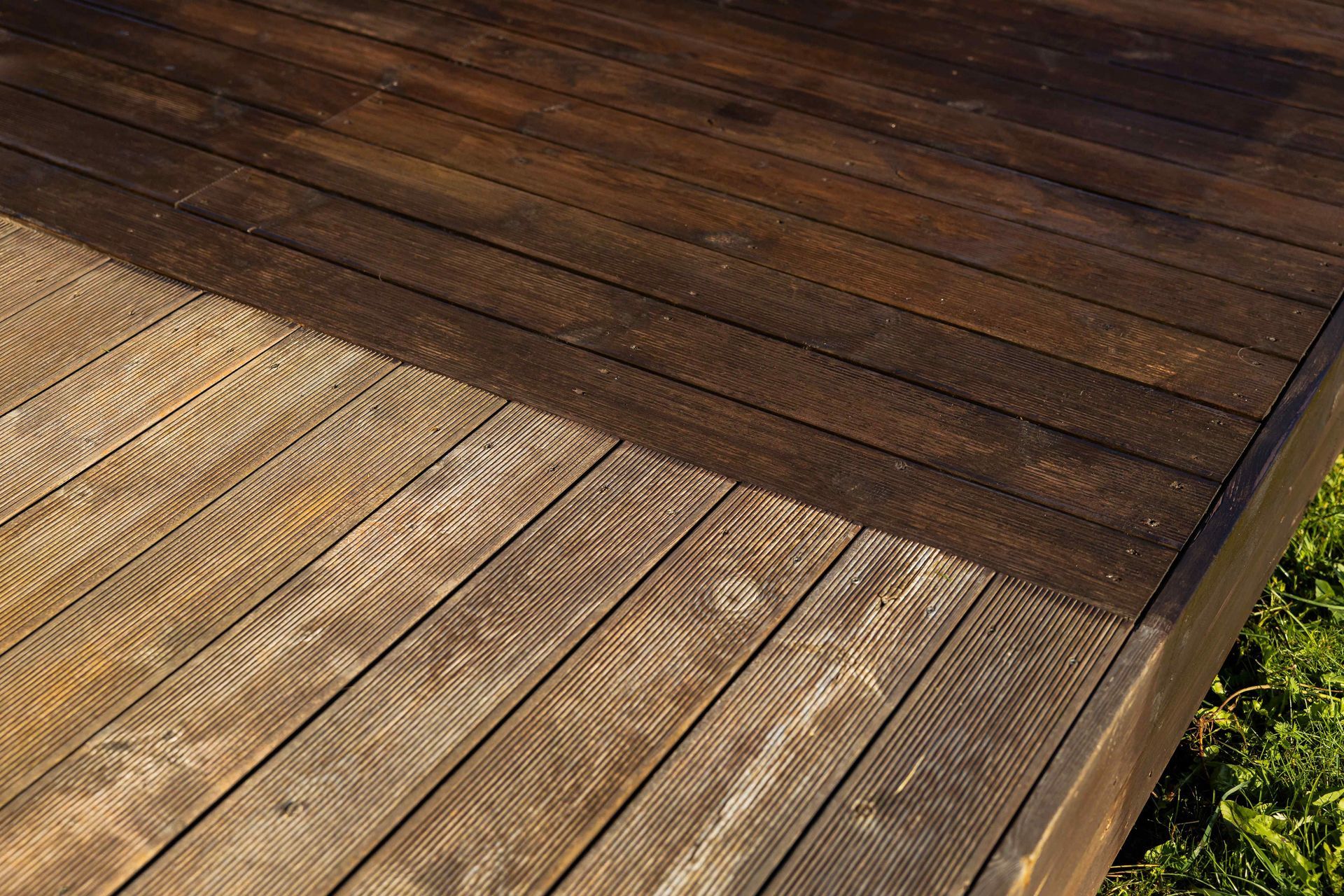 Wooden deck showing a contrast in colors; one half is dark brown, the other is weathered light brown.
